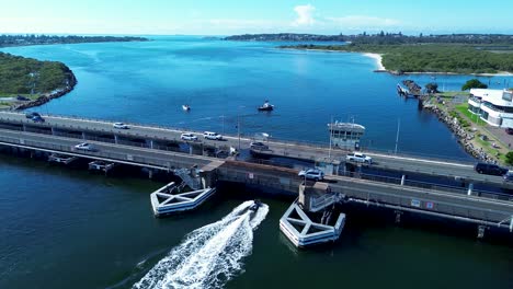 Landschaftsaufnahme-Eines-Bootes,-Das-Unter-Einer-Autobahnbrücke-Im-Swansea-Channel-Inlet-River-Belmont-Australien-Unterwegs-Ist,-Reisetransport,-Drohnenluftaufnahme