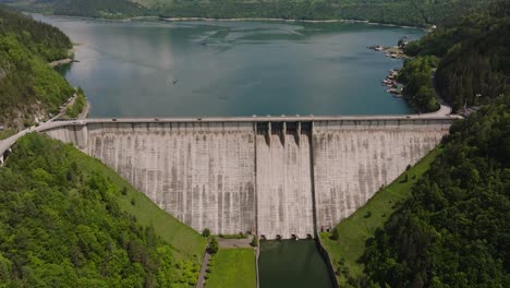 Dam-and-water-reservoir-surrounded-by-green-forests,-panoramic-aerial-view