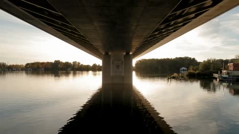 Drone-captures-a-tranquil-European-river,-showing-the-underside-of-a-bridge