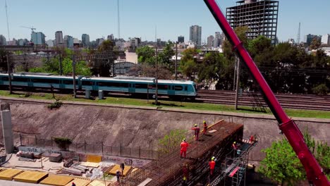 Train-passes-by-construction-site-by-Buenos-Aires-skyline,-aerial-push-in