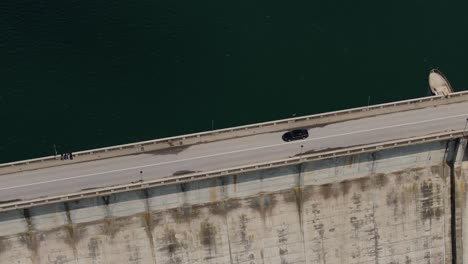 Black-car-driving-on-a-dam,-between-a-water-reservoir-and-deep-valley,-tracking-drone-close-up-shot