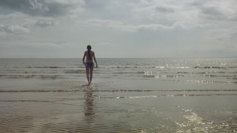Young-girl-walking-out-to-sea-water,-warm-sunlight-scene,-slow-motion