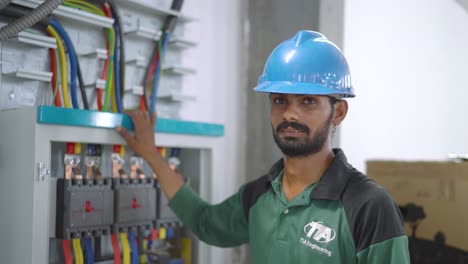 Ingeniero-Paquistaní-Vestido-De-Azul-De-Pie-Junto-A-La-Caja-De-Control-En-El-Almacén-De-La-Fábrica