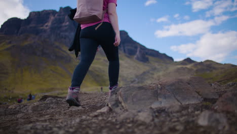 Mujer-Mochilero-Caminando-En-La-Campiña-Escocesa,-El-Storr-En-Segundo-Plano.