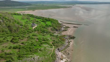 House-on-remote-green-coastline-with-pointed-manmade-rock-structure-jutting-out-into-receding-tide-on-bright-day-in-Spring-at-Jenny-Brown's-Point,-Silverdale,-Lancashire,-England,-UK