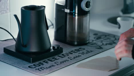 Folding-up-the-Paper-for-Filter-Coffee-Chemex-with-barista-water-kettle-and-grinder-in-the-background-in-slow-motion