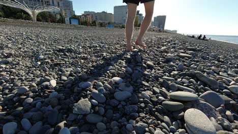 Man-walk-on-rocky-beach-full-of-pebbles,-scene-captures-a-moment-of-leisure-in-Batumi-Georgia