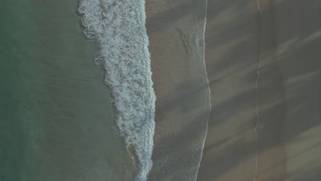 Ocean-waves-calmly-wash-over-sand-beach,-top-down-aerial-push-in