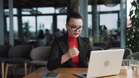 Eine-Schöne-Junge-Frau-In-Business-Kleidung-Sitzt-In-Einem-Stilvollen-Restaurant-Und-Tippt-Wütend-Auf-Einem-Laptop,-Der-Nicht-Mehr-Funktioniert-Und-Eingefroren-Ist