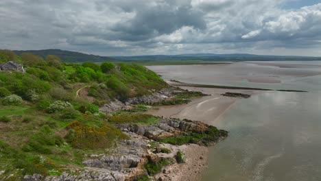 Volando-Sobre-La-Escarpada-Costa-Rocosa-Hacia-El-Horizonte-Nublado-En-Un-Brillante-Día-De-Primavera-Mientras-La-Marea-Retrocede-En-Jenny-Brown&#39;s-Point,-Silverdale,-Lancashire,-Inglaterra,-Reino-Unido.