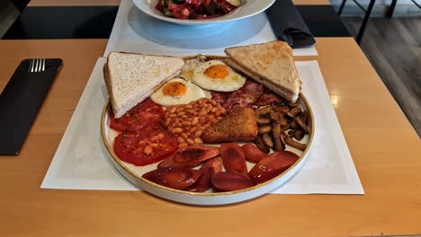 Se-Sirve-Un-Desayuno-Inglés-Completo-En-Un-Plato-Que-Incluye-Huevos-Fritos,-Tostadas,-Alubias,-Tomates-Asados,-Salchichas,-Champiñones-Y-Croquetas-De-Patata.