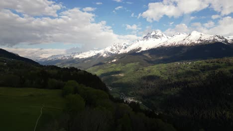 Aerial-view-of-the-valley-in-Obersaxen,-Graubünden,-Switzerland,-encircled-by-a-mountainous-range-with-snow-covered-peaks