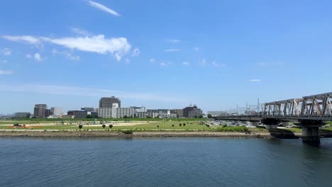 Un-Pintoresco-Parque-Junto-Al-Río-Junto-A-Un-Puente-Bajo-Un-Cielo-Azul-Claro-En-Un-Día-Soleado