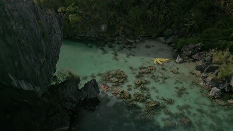 Aerial-pull-out-of-kayaks-in-still-water-by-green-mountain-landscape,-Philippines