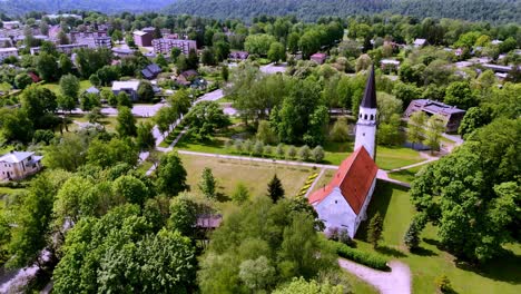 Latvia,-Europe---Panorama-of-the-Sigulda-Evangelical-Lutheran-Church-Nestled-in-the-Heart-of-a-Lush-Green-Park---Aerial-Drone-Shot