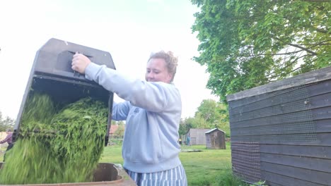 Young-woman-emptying-grass-cuttings-into-compost-recycle-bin