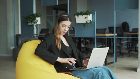 pretty-young-woman-in-business-attire-sits-with-her-laptop-in-a-stylish,-modern-coworking-office,-receiving-a-joyful-message-about-winning