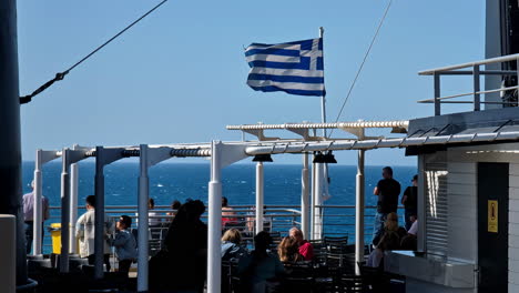 La-Gente-Disfruta-De-Un-Viaje-En-Ferry-Con-Vista-Al-Mar-Y-La-Bandera-Griega-Ondeando-En-El-Viento.