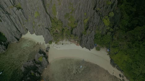 Rocky-forested-cliffs-and-sand-beach-in-Philippines,-aerial-pull-out