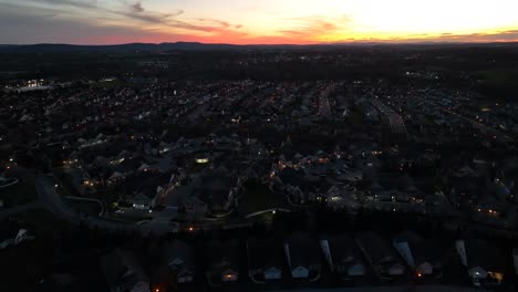 Dusk-settles-over-a-sprawling-suburban-neighborhood-with-house-lights-twinkling-under-a-colorful-sky