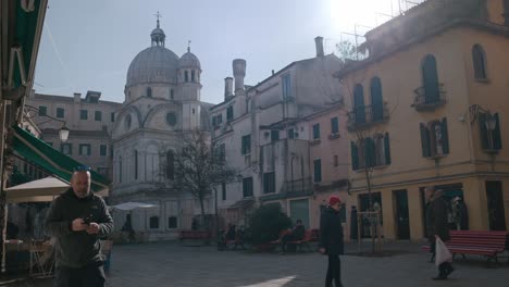 Ruhiger-Platz-In-Venedig-Mit-Der-Beeindruckenden-Kirche-Santa-Maria-Dei-Miracoli-Im-Hintergrund,-Menschen,-Die-Spazieren-Gehen-Und-Auf-Bänken-Sitzen,-Heitere-Atmosphäre-Der-Stadt