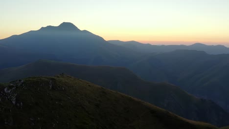 Shot-of-a-drone,-flying-over-the-crest-of-a-mountain-with-a-sunset-in-the-background