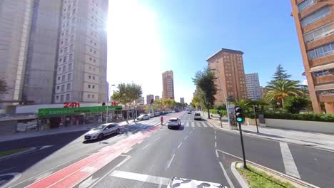 Coches-Acelerando-En-Una-Carretera-Vacía-Con-Un-Alto-En-El-Semáforo-Durante-Un-Día-Soleado-En-La-Ciudad-Rodeada-De-Edificios-Altos,-Tiendas-Y-Comercios.