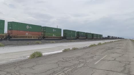 Freight-train-transporting-green-containers-along-Interstate-80-freeway-in-Utah