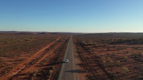 Aerial:-Drone-shot-tracking-a-white-4WD-vehicle-closely-as-it-drives-along-an-empty-tarmac-road-within-the-outback,-north-of-Broken-Hill,-Australia
