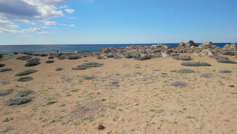 A-sandy-coastal-area-with-sparse-vegetation-at-the-Tombs-of-the-Kings-in-Pafos,-Cyprus,-under-a-blue-sky