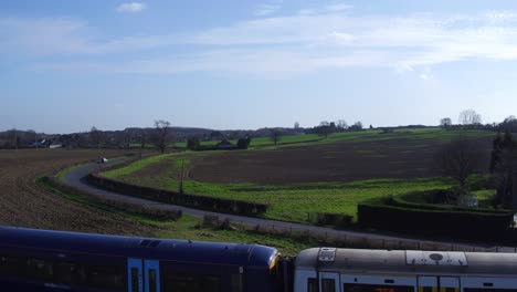 Toma-Aérea-En-Ascenso-De-Un-Tren-De-Cercanías-Del-Sureste-En-El-Campo-Cerca-De-Ashford,-Kent