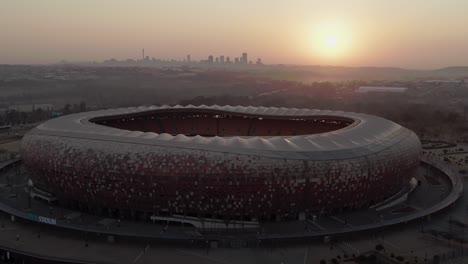 FNB-Stadion,-4K-Drohnenluftaufnahme,-Pushing-Inn-Bei-Sonnenaufgang-Mit-Johannesburg-CBD-In-Der-Ferne_03