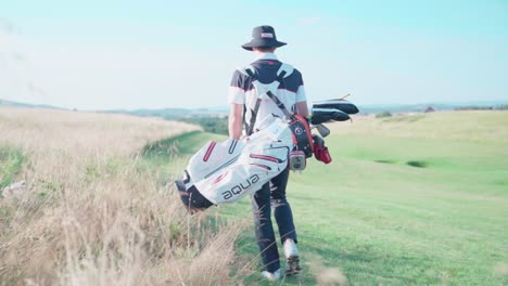 Golfista-En-El-Campo-De-Golf-Llevando-Una-Bolsa-Con-Palos,-Pistas-De-Cámara-Aunque-En-El-Campo