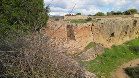 A-closer-view-of-the-archaeological-site-at-the-Tombs-of-the-Kings-in-Pafos,-Cyprus,-with-rocky-terrain-and-ancient-structures