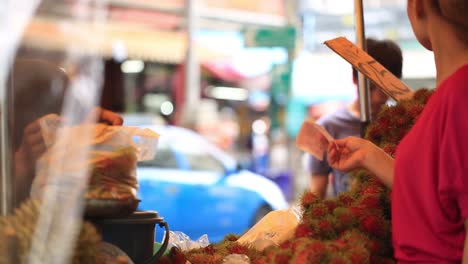 Eine-Frau-Kauft-Ein-Kilo-Rambutanfrüchte-Von-Einem-Männlichen-Händler-In-Bangkok,-Thailand---Mittlere-Aufnahme