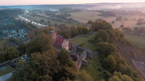 Ruin-Isenburg-with-vibrant-sunrise-over-misty-Ruhr-river,-orbit-drone-aerial