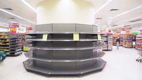 Shoppers-wear-face-masks-walk-past-empty-supermarket-shelves,-usually-stocked-with-toilet-paper