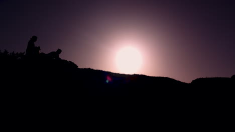 Dos-Amigos-Cargando-Cajas-Mientras-El-Sol-Sale-En-Un-Cielo-Púrpura