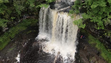 People-emerging-from-behind-Breacon-Beacons-Welsh-woodland-cascading-waterfall-aerial-orbit-right