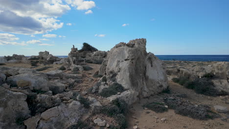 A-rocky-coastal-landscape-at-the-Tombs-of-the-Kings-in-Pafos,-Cyprus,-with-the-sea-in-the-background-under-a-clear-blue-sky