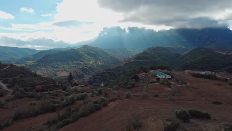 Blick-Auf-Die-Berge-Von-Montserrat-Und-Marganell-Mit-Verstreuten-Gebäuden-Und-Sonnenlicht,-Das-Durch-Die-Wolken-Strömt