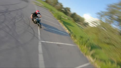 Eine-FPV-Drohne-Macht-Eine-Fassrolle,-Während-Sie-Sich-Einem-Stunt-Biker-Nähert,-Der-In-Einer-Kurve-Driftet.-Gefilmt-Mit-60 fps