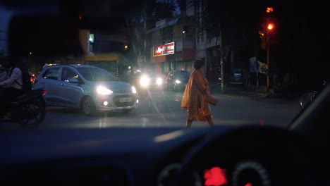 Woman-Crossing-The-Busy-Road-With-Transport-Vehicles-Slowly-Moving-Through-Intersection-During-The-Night-In-Delhi,-India