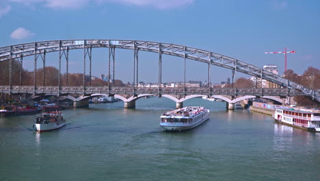 A-large-and-a-small-ship-cross-underneath-the-Viaduc-d'Austerlitz-in-Paris-on-a-sunny-day-at-noon