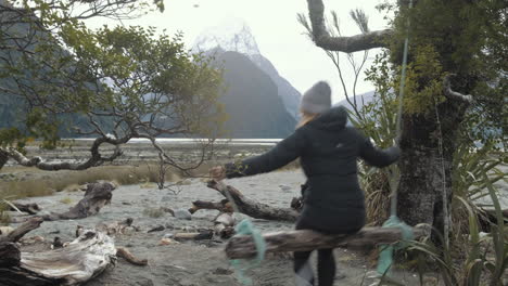 Chica-Balanceándose-En-Un-Columpio-De-Madera-Con-Montañas-Cubiertas-De-Nieve-En-El-Fondo