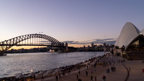 Day-to-Night-timelapse-of-walking-people-at-boardwalk-and-Opera-House-with-Bridge-in-background-in-Sydney