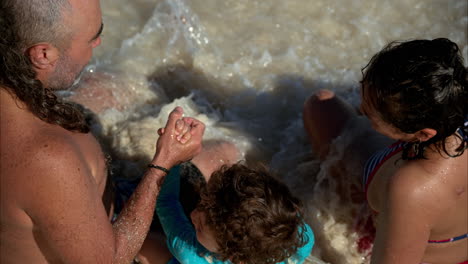 Zeitlupe-Einer-Dreiköpfigen-Mexikanischen-Hipster-Familie,-Die-Im-Sand-Sitzt,-Von-Den-Wellen-Getroffen-Wird-Und-Einen-Warmen-Tag-In-Cancun-Genießt