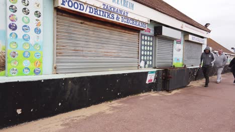 La-Gente-Con-Sobrepeso-Camina-Delante-De-Una-Tienda-De-Comida-Para-Llevar-Cerrada-Y-Deteriorada.