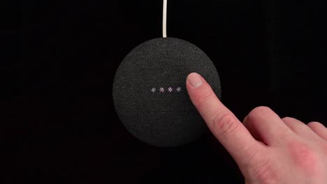 Person-pressing-a-Google-Nest-Home-Mini-smart-speaker-with-built-in-Google-Assistant-on-a-black-background