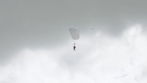 A-tandem-jump-Skydivers-with-open-Parachutes-slowely-glide-down-to-earth-and-lands-behind-a-plane